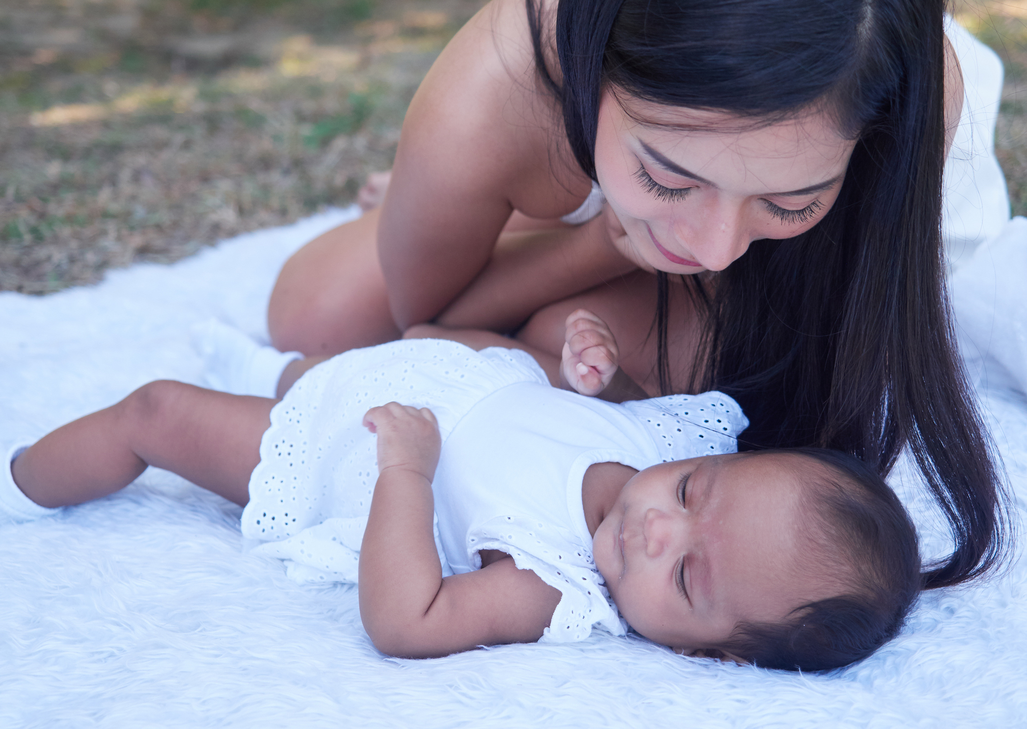 Mom and infant baby outside on blanket, wearing white.