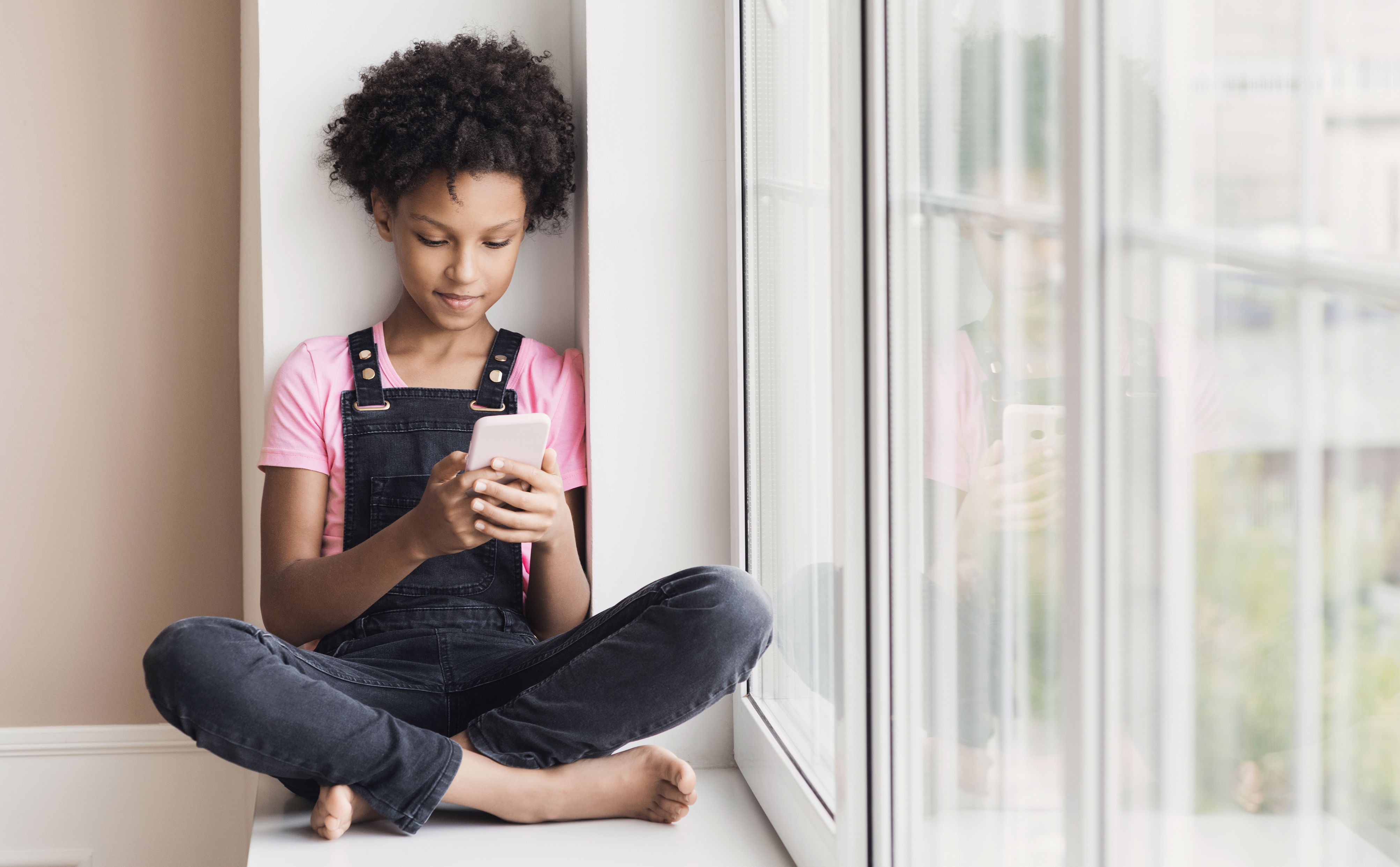 Preteen girl sitting down at window looking at smart phone