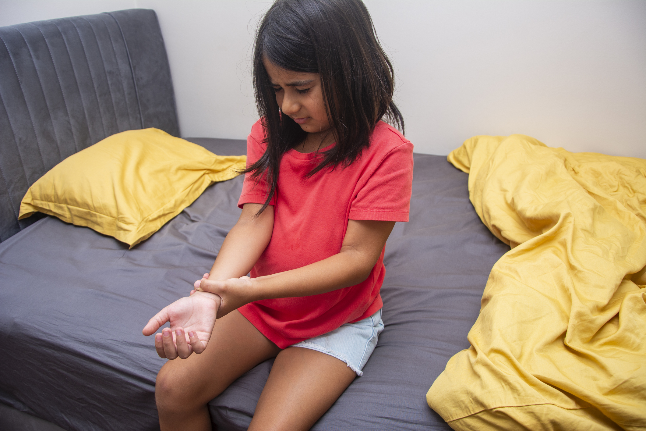 Little girl, maybe with carpal tunnel syndrome, sitting on bed grabbing wrist in pain