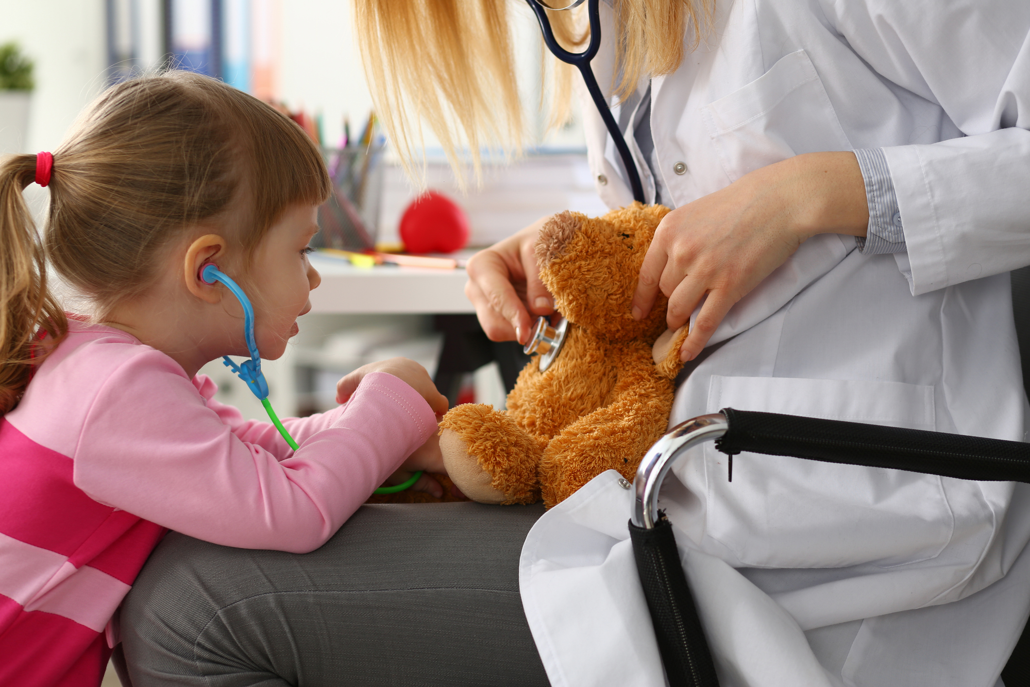 Young girl listening to teddy bear's heart on doctor's lap
