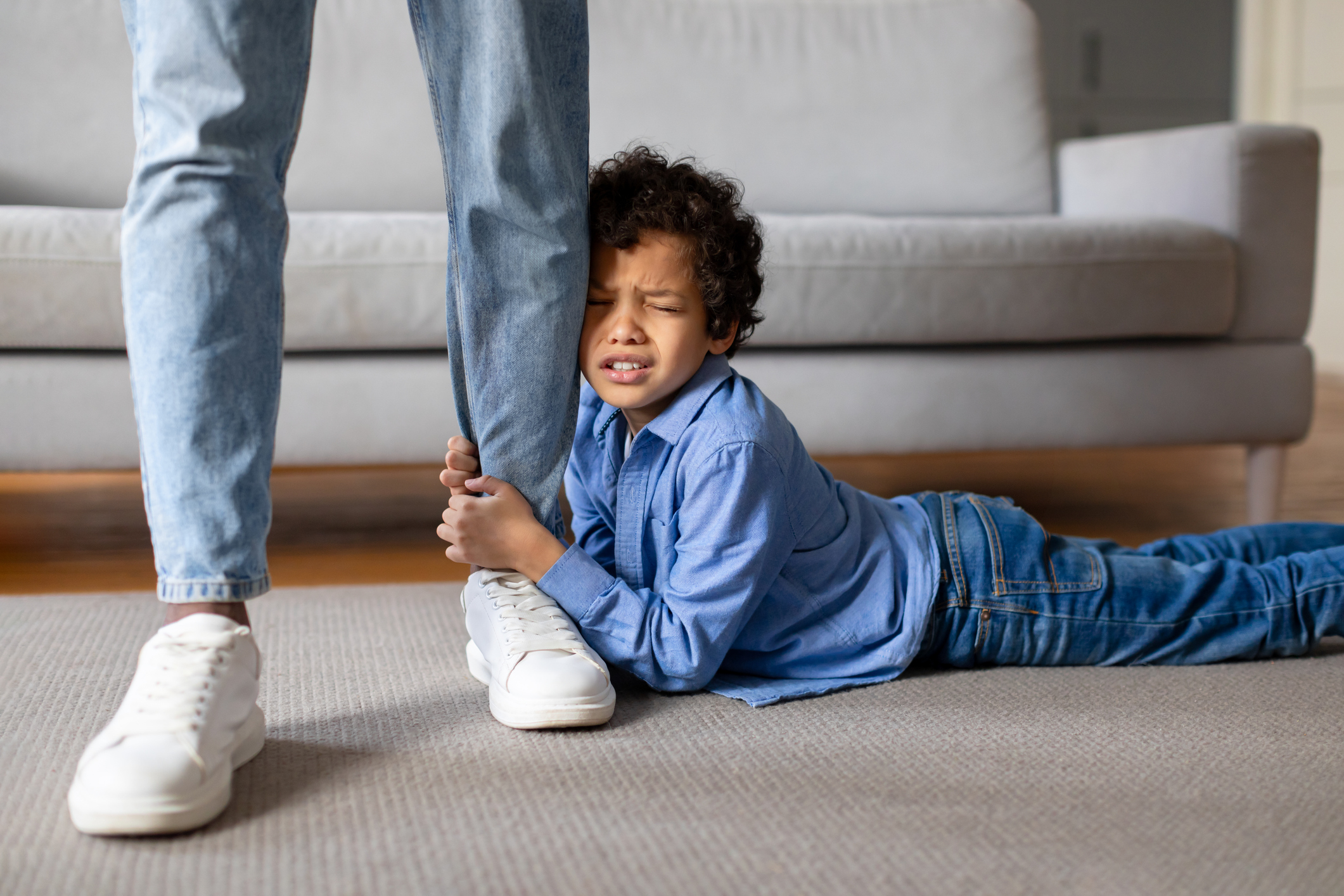 Young boy having tantrum, clinging to parent's leg, laying on floor