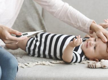 Mom holding thermometer next to infant on floor