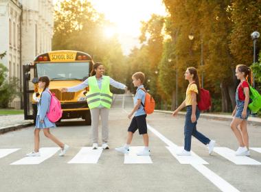 Crossing guard and four preteens crossing street in front of school bus. Back to school bus, road and bike safety 