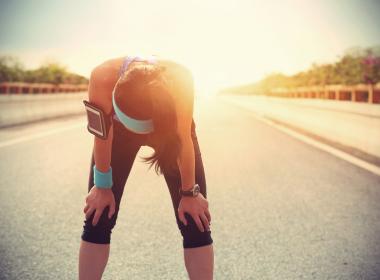 Young adult female runner bent over, overheated, outside