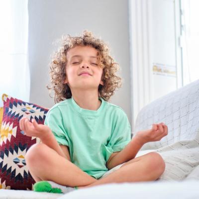 Young boy, practicing meditation on sofa, eyes shut, smiling