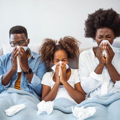 Family of 3, sneezing into tissues on couch.